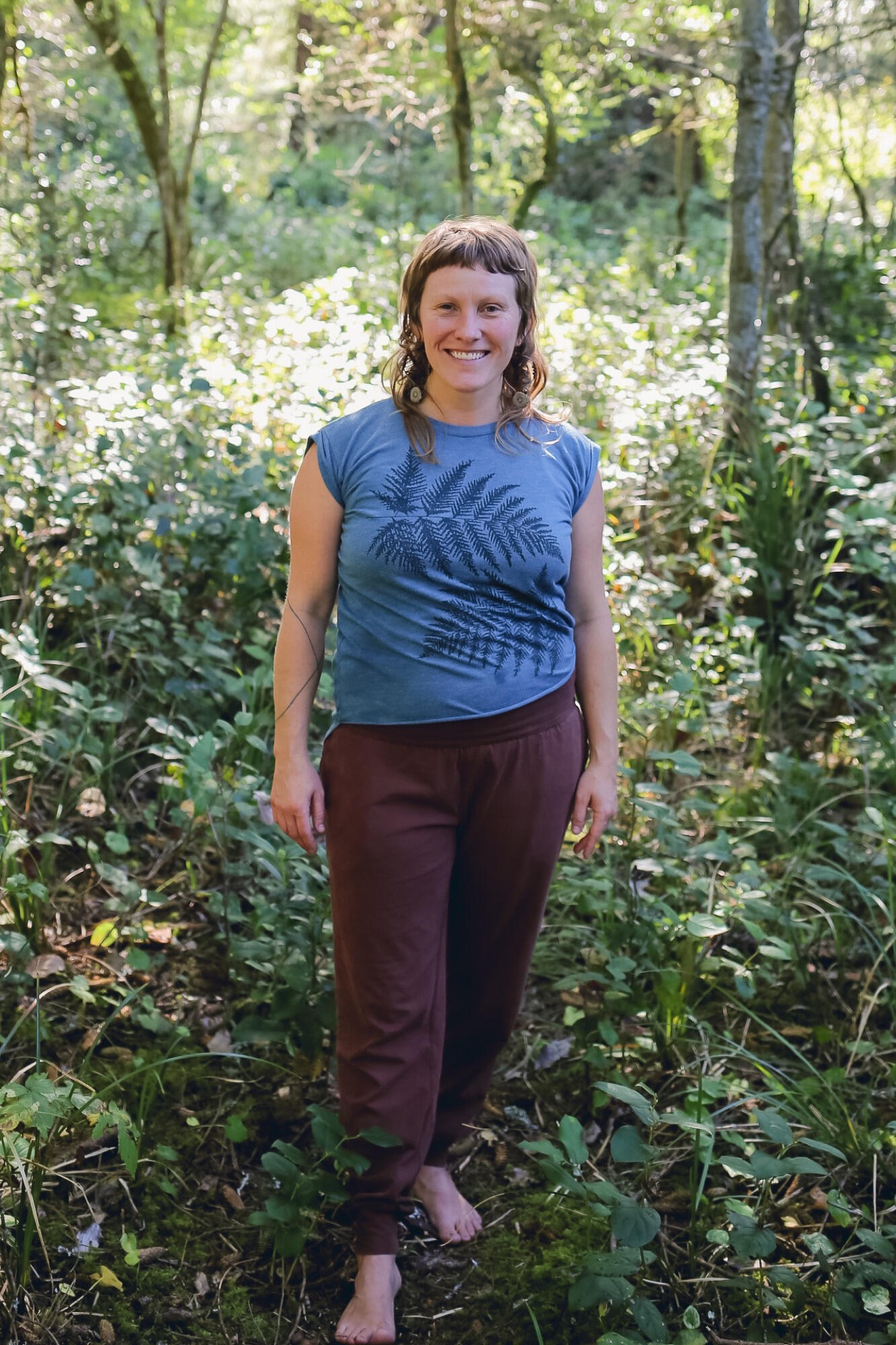 Fae, the massage therapist behind Mycelial MindBody, smiling in a sunlit forest
